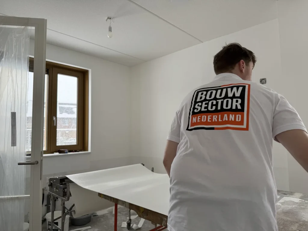 Behanger van Bouwsector Nederland met een baan vlies op de plakmachine in een nieuwbouwkamer