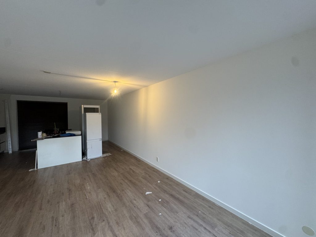 Open woonkamer met keukenblok en een lange, egaal witte wand in een nieuw appartement