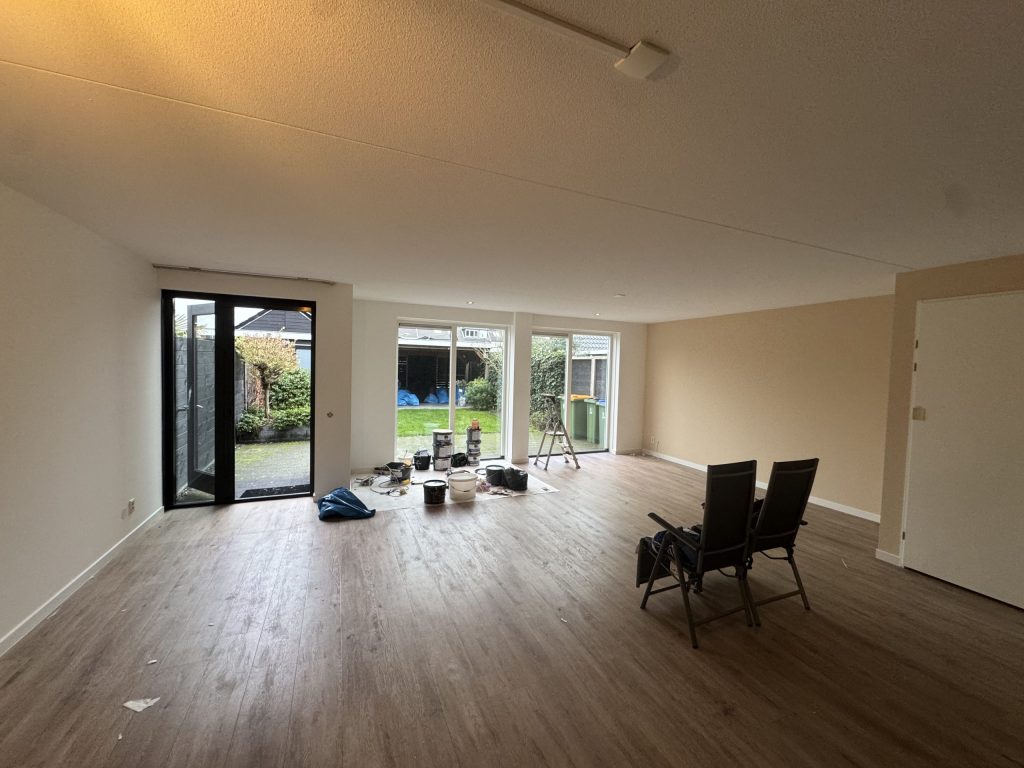 Lege woonkamer met tuindeuren, verfemmers en een trapje tijdens het afwerken van de wanden