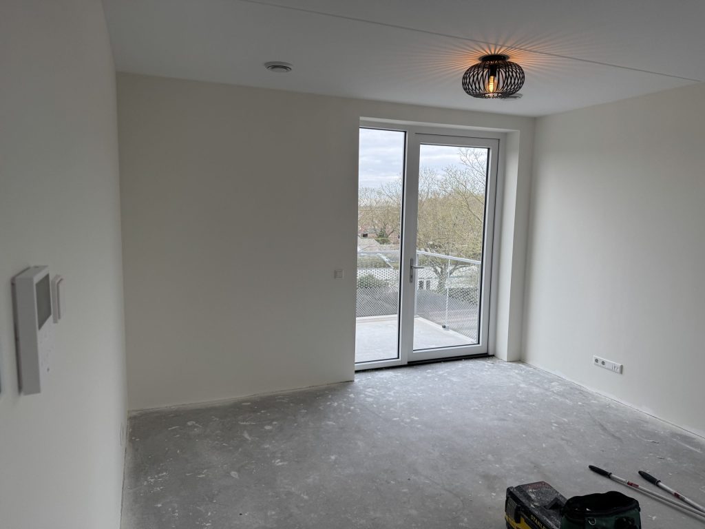 Lege kamer in een nieuw appartement met balkondeuren en kale betonvloer, kort na de oplevering